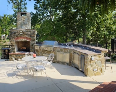 Outdoor fireplace made of stone with stone kitchen counter, built-in grill, and accessories